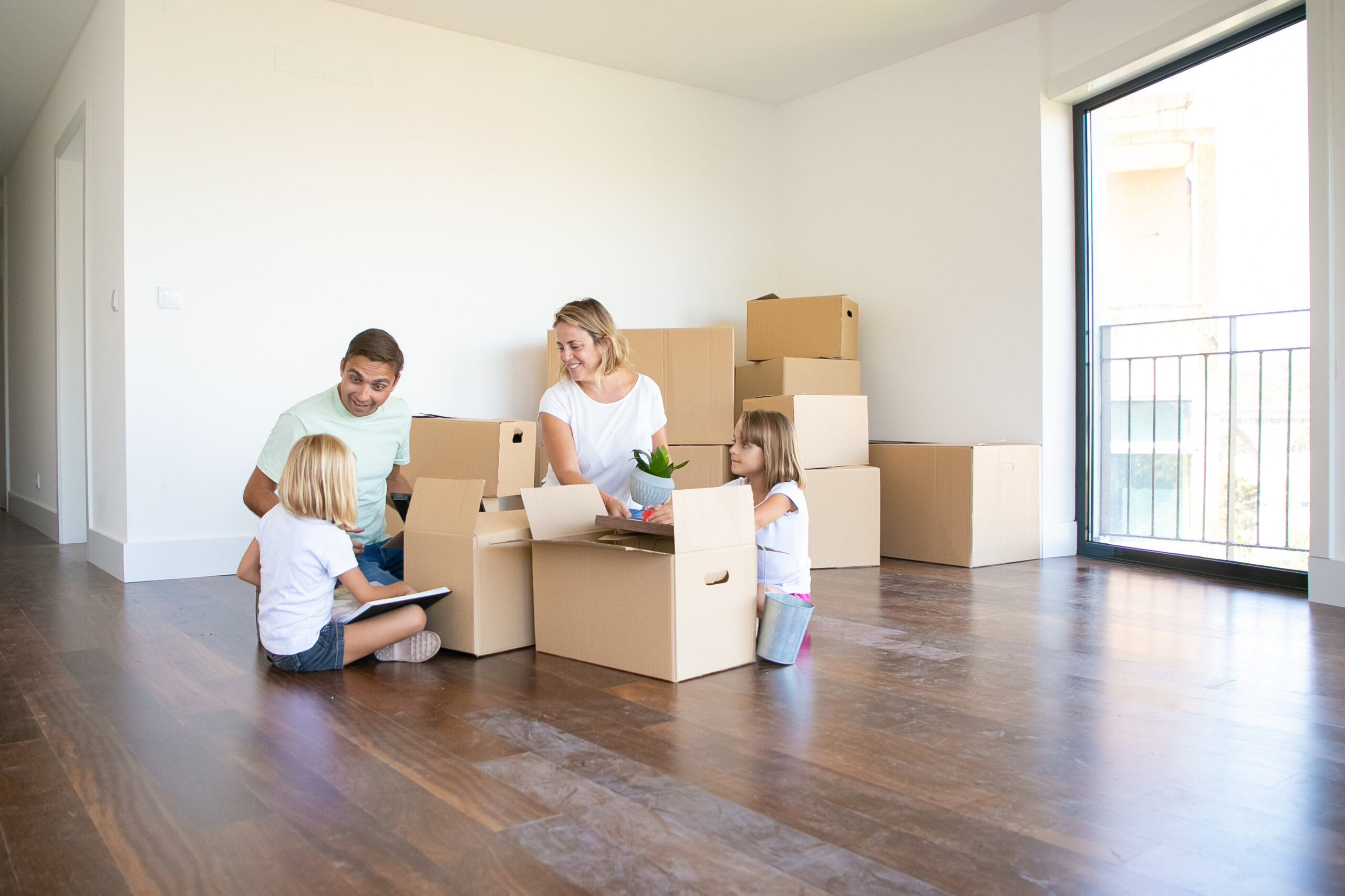 happy parents two kids moving into new empty apartment sitting floor near open boxes